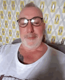 a man with glasses and a tattoo on his chest is sitting on a couch