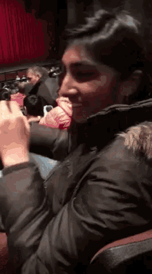a woman in a black jacket is smiling while sitting in an auditorium
