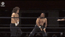 a man is kneeling in a wrestling ring while another man stands in the corner .