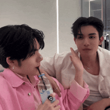 a man in a pink jacket is drinking from a bottle with a straw that has the letter c on it