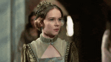 a woman in a green dress with a crown on her head is looking at the camera .