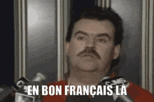 a man with a mustache is speaking into a microphone with the words en bon francais la above him