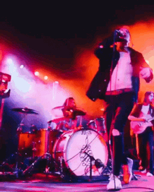 a man singing into a microphone in front of a drum set that says ' drums ' on them