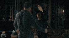 a man in a plaid shirt is hugging another man in a living room with a prime logo on the corner