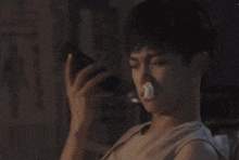 a young man with a bandage on his nose is looking at his phone .