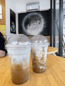 two cups of coffee are on a table in front of a moon painting