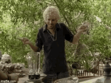 a man with curly hair is standing in front of a blender and a table .