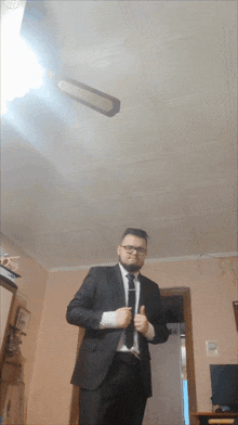 a man in a suit and tie giving a thumbs up in front of a ceiling fan