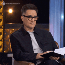 a man wearing glasses is sitting in a chair with a book in his hand and the hashtag #cbcdragonsden above him