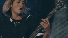 a man in a skn 01 shirt playing a guitar