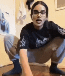 a woman wearing glasses is squatting on the floor .