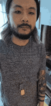 a man with a beard and long hair is wearing a gray shirt and a hat .