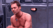 a shirtless man is sitting in a room with his arms outstretched and talking .