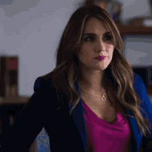 a woman wearing a blue jacket and a pink shirt has a necklace with the letter o on it