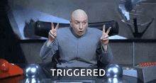 dr. evil is giving a peace sign while sitting at a desk in front of a computer .