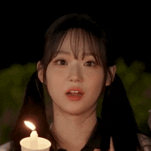 a young girl with pigtails is holding a lit candle in her hand .