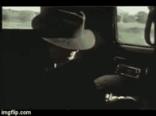 a man in a hat is sitting in a car looking out the window .