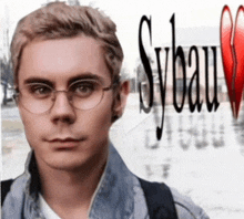 a young man wearing glasses stands in front of a sybau sign