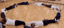 a group of people are laying in a circle on the floor in a gym .