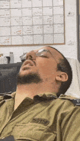 a man in a military uniform is sleeping in front of a whiteboard with a calendar on it