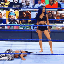 a woman is standing in a wrestling ring next to a woman laying on the floor .