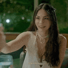 a woman is sitting at a table with a glass of wine and a necklace on her neck .