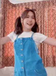 a girl wearing overalls and pigtails is dancing in a room .