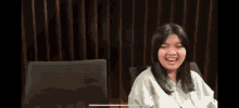 a young woman is sitting in a chair and smiling while a man throws a pink object in the background .