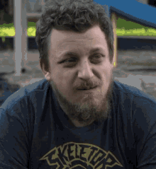 a man with a beard is wearing a blue shirt that says skeletor