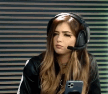 a woman wearing headphones and a microphone looks at her phone .
