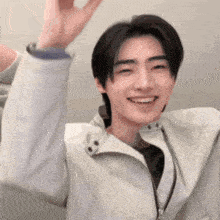 a young man wearing a white jacket is smiling and waving his hand .