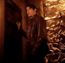 a man in a brown leather jacket is standing in front of a door in a dark room .