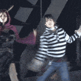 a man in a striped shirt is dancing next to a woman in a purple top