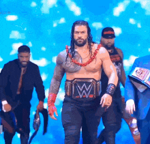 a group of wrestlers are walking on a stage and one of them has a w belt on his belt .