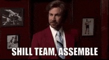 a man in a red suit and tie is holding a piece of paper in his hand and saying `` shill team assemble '' .