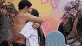 a shirtless man is hugging a woman in front of flowers and a sign that says bbbo
