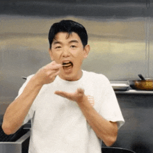 a man in a white t-shirt is eating a piece of food