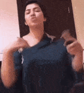 a woman in a blue shirt is blowing a kiss while holding a cell phone