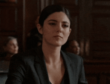 a woman is sitting in a courtroom wearing a black suit and a black shirt .