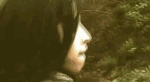 a woman with a mask on her face is standing in front of a brick wall in the woods .