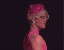 a man in a pink dress and wig is standing in the dark .