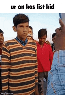 a boy in a striped shirt is standing in front of a crowd of people .