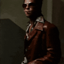 a man wearing sunglasses and a brown leather jacket is smoking a cigarette .
