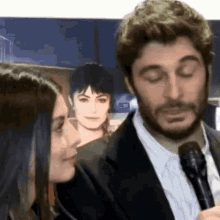 a man in a suit and tie is talking into a microphone while a woman looks on