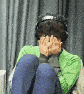 a person wearing headphones covering their face with their hands .