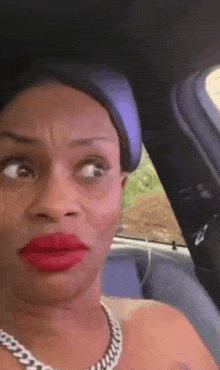a woman with red lipstick and a necklace is sitting in a car making a funny face