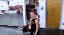 a girl with a bow in her hair is sitting in a dance studio eating a snack .