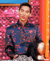 a man in a floral shirt is holding a mannequin 's head and making a funny face .