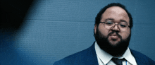 a man with glasses and a beard wears a blue suit