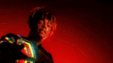 a man with dreadlocks is standing in front of a red background and holding a light in his hand .